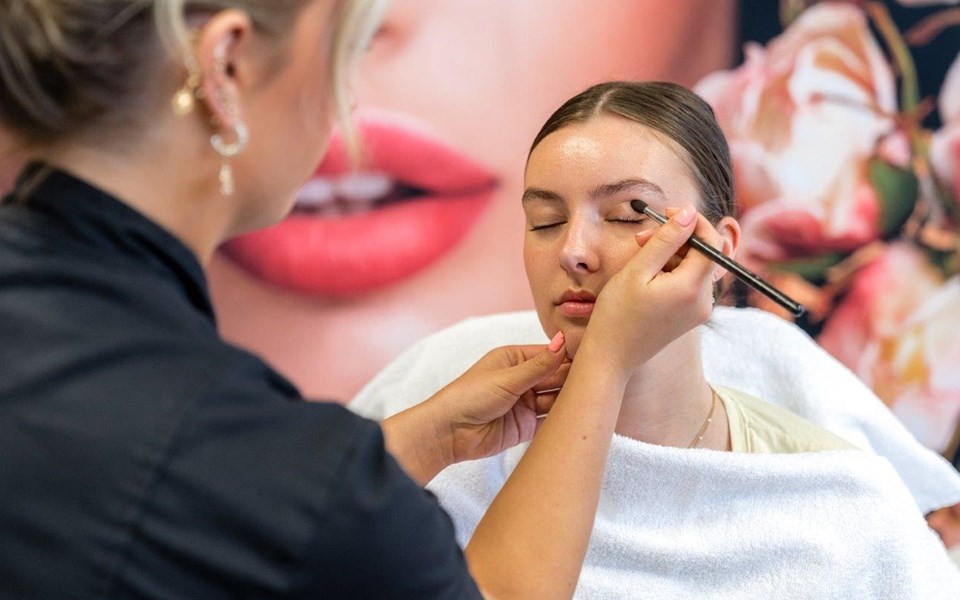 Student schoonheidsspecialist brengt oog make-up aan bij klant