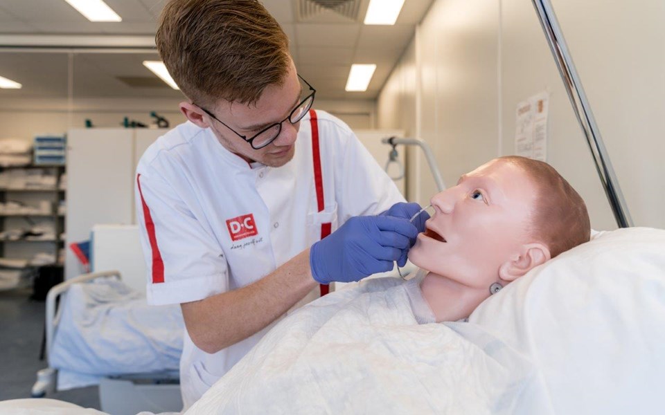 Student opleiding verpleegkundige oefent met sonde bij volwassen pop op bed. 