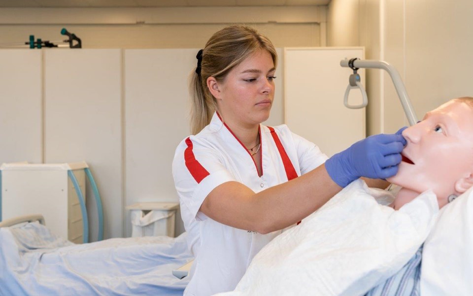 Student Verpleegkunde oefent met sonde bij volwassen pop in bed. 