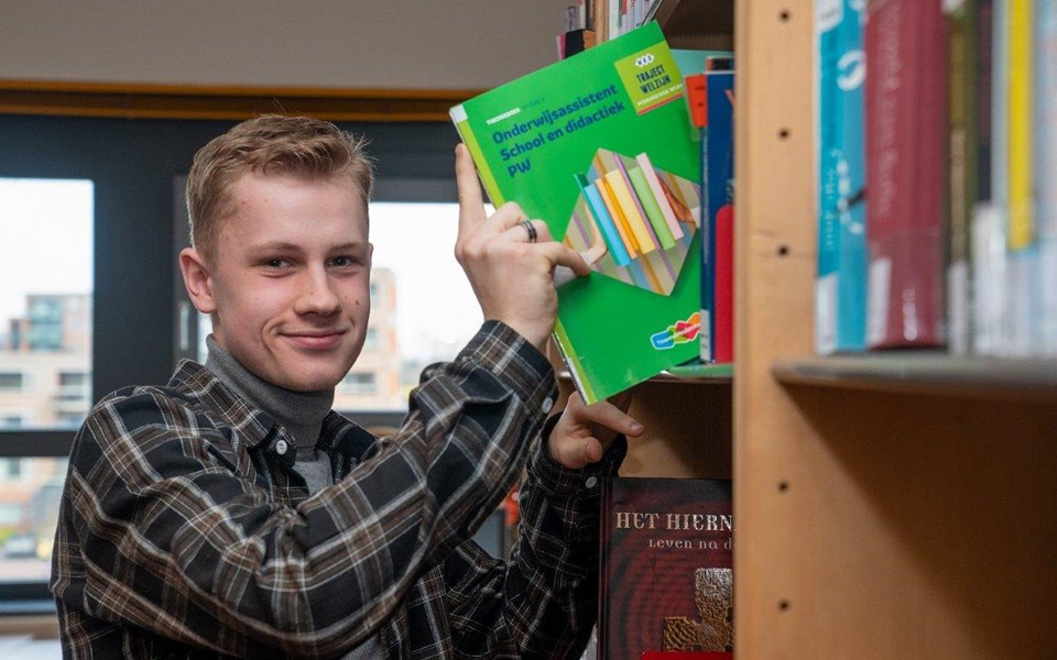 Student haalt boek onderwijsassistent uit grote open boekenkast. 