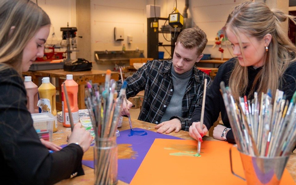 Drie studenten opleiding onderwijsassistent zijn aan het verven op gekleurde papieren. 