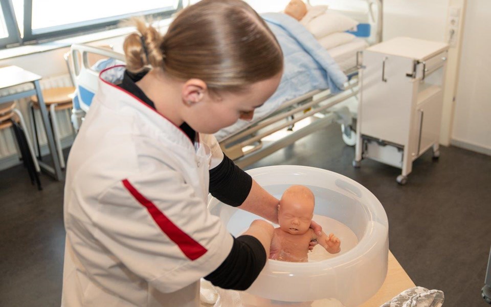 Student opleiding Helpende wast babypop in tummy tub.
