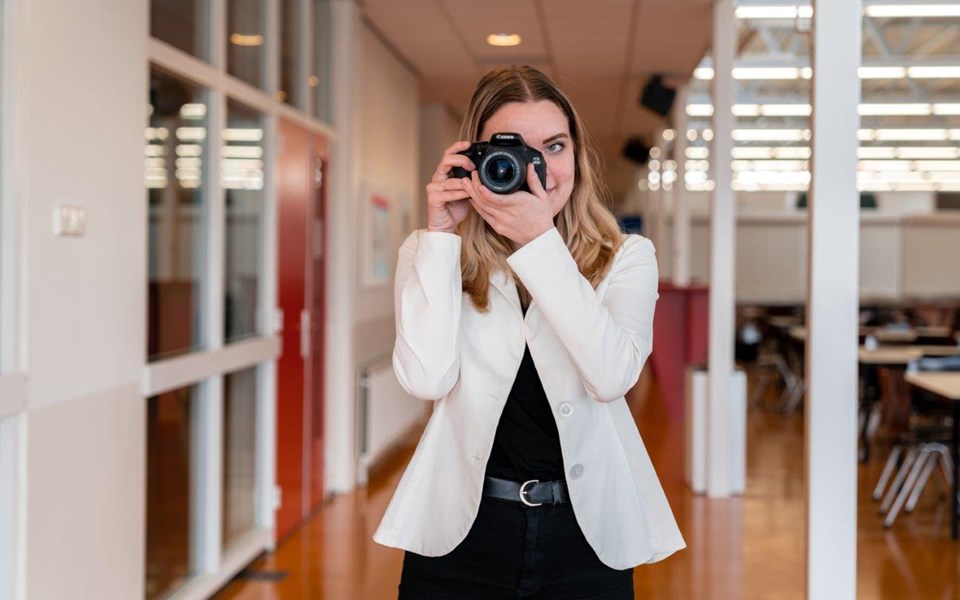 Mediavormgeving student heeft fotocamera voor haar rechteroog en draait aan de lens