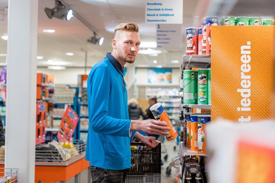 Man in supermarkt zet doos pringles in het schap.