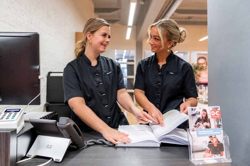 Schoonheidsverzorging + Salon, Iris Sijbom 2022 (21) Twee studenten schoonheidsspecialist staan achter de balie en wijzen iets aan in de agenda