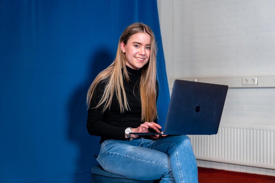 Mediavormgever, Iris Sijbom 2022 (18) Student mediavormgeving zit met laptop op schoot tegen blauwe muur aan