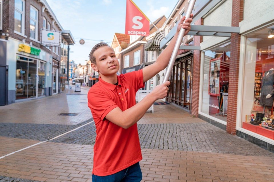 Jongen hangt vlag van winkel buiten op.