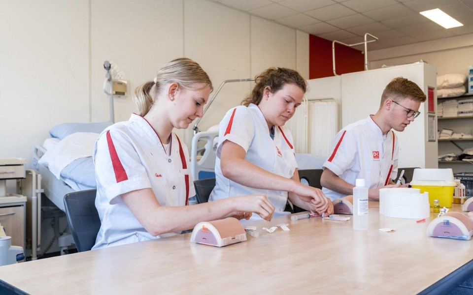 Drie studenten verpleegkunde oefenen met naalden en prikken.