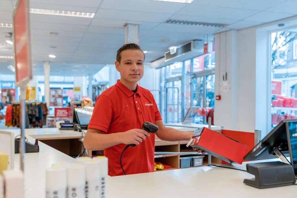 Jongen achter kassa winkel scant schoenendoos.