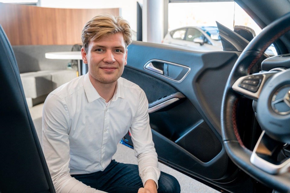 Man zit gehurkt bij openstaande auto.
