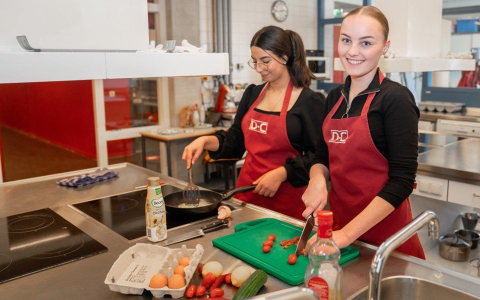 Twee studenten Helpende snijden groent en bakken ei in keuken. 