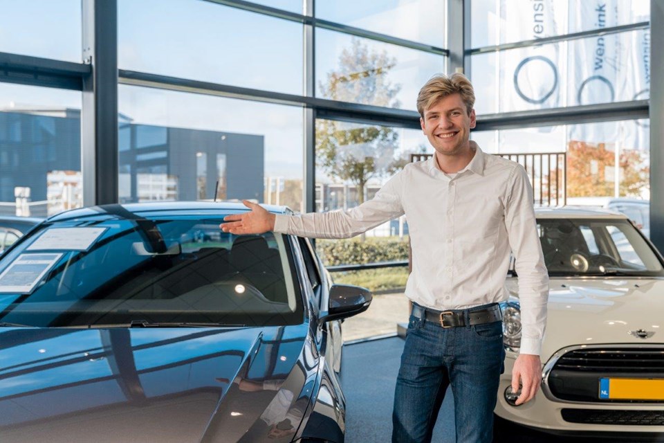 Man wijst auto aan in showroom.