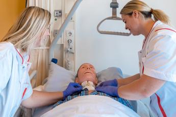 Twee verpleegkundigen helpen man die in bed ligt.