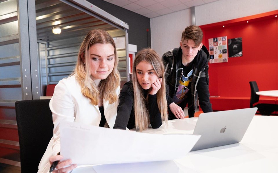 Drie studenten mediavormgeving kijken samen naar een groot wit A3 papier