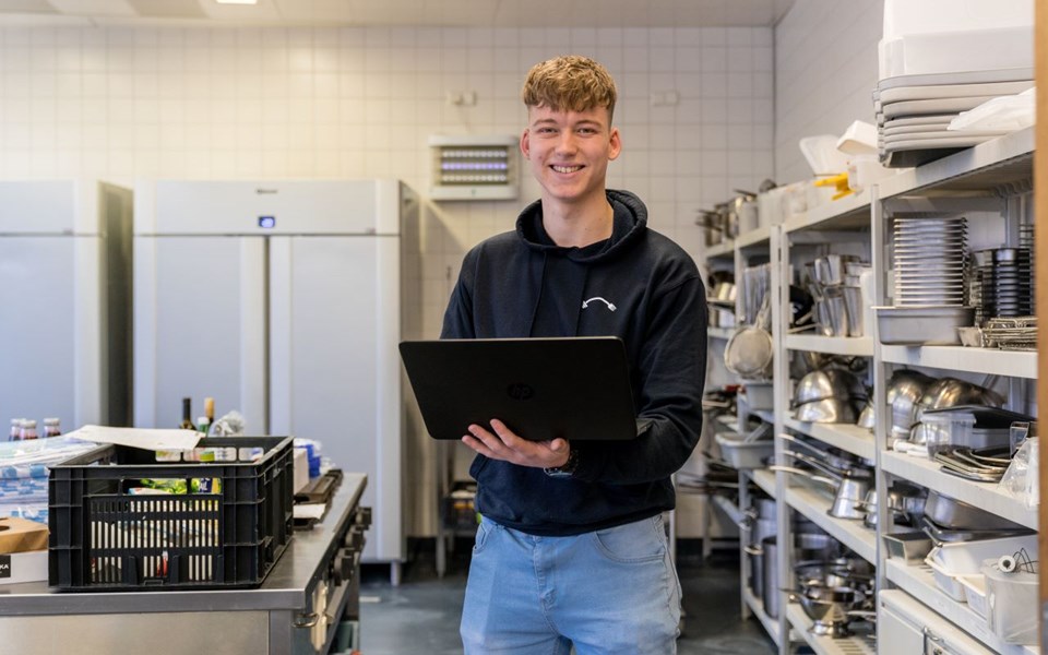 E-commerce student staat in keuken met laptop in zijn hand