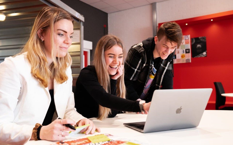 Drie studenten mediavormgeving zitten lachend achter een laptop