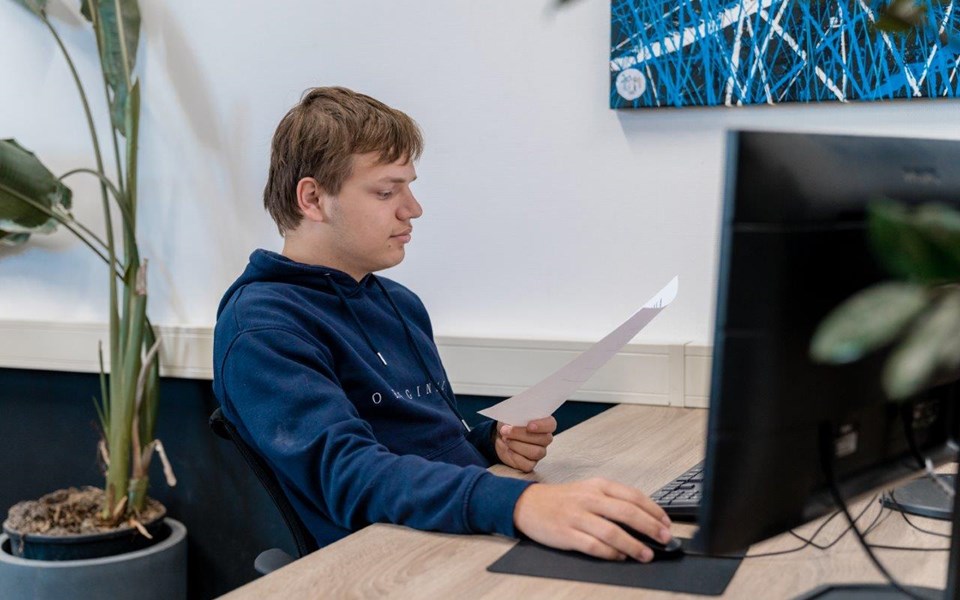 Jongens leest papier en zit achter computer.