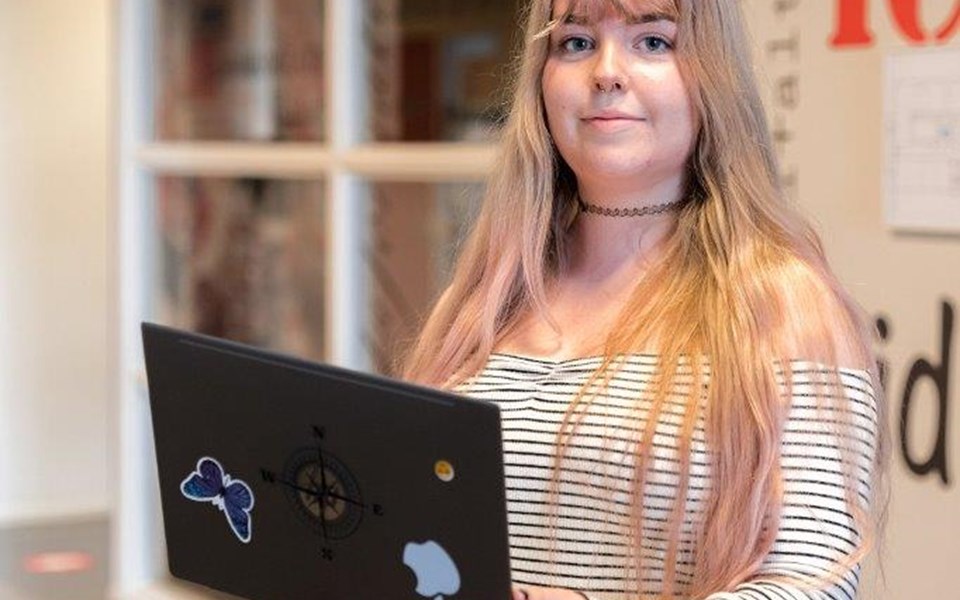 Student ICT staand in de gang met laptop in handen