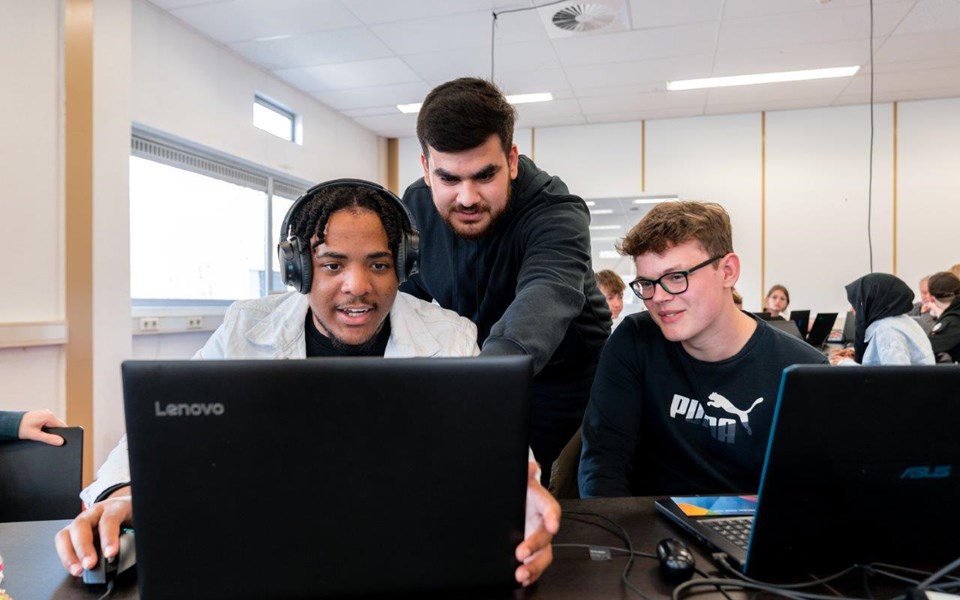 Drie studenten Software Developer kijken naar één beeldscherm en wijzen daarop iets aan