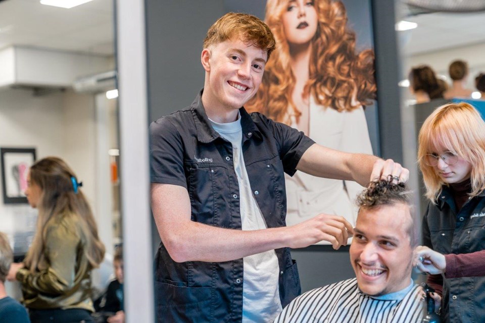 Drie kappers aan het werk in salon met lachende klant in stoel.