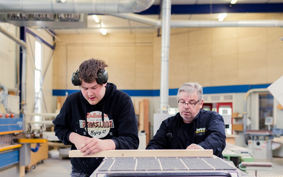 Student en leraar werken met hout snijmachine in werkplaats