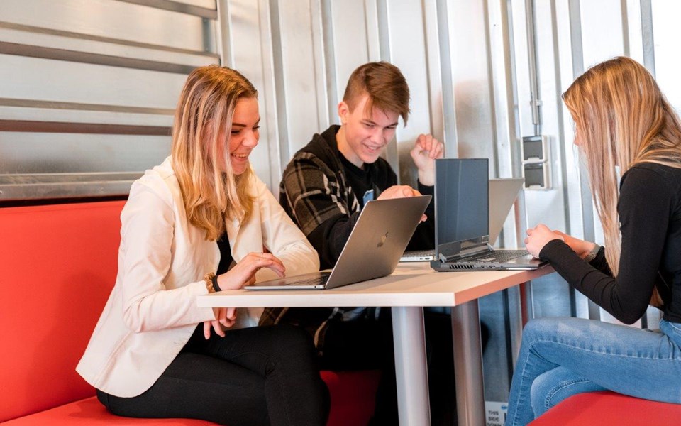 Drie mediavormgevers in opleiding zittend aan het werk op hun laptop bij tafel