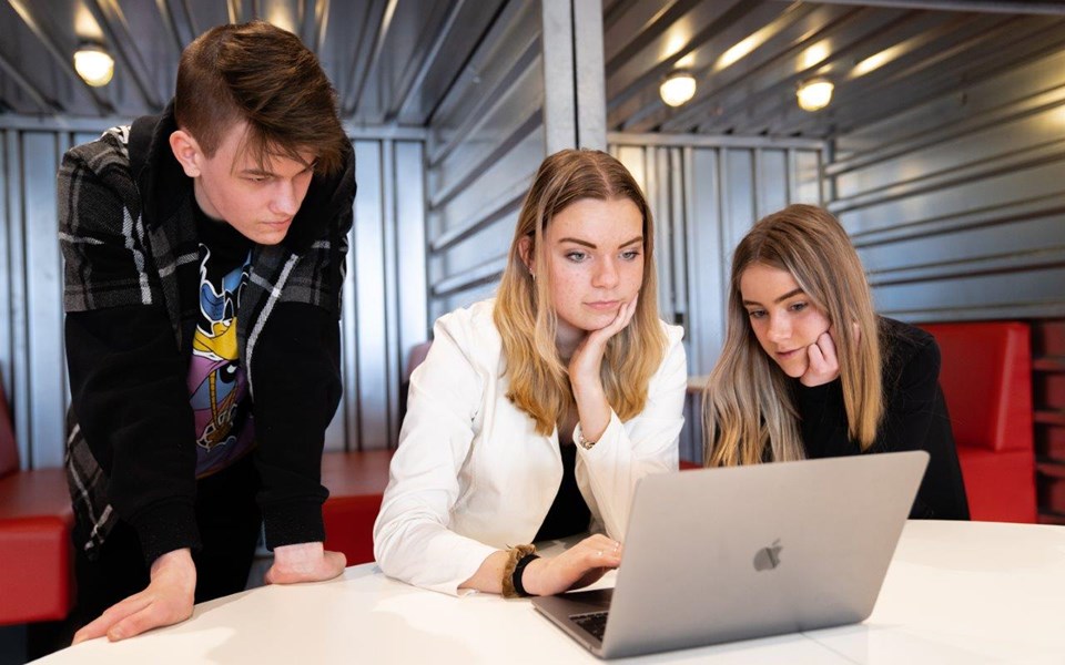 Drie mediavormgevers in opleiding kijken samen naar het scherm van een laptop