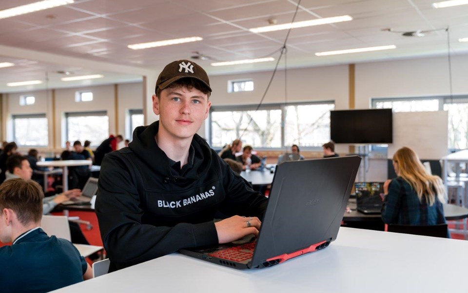 Software Developer in opleiding zit met laptop aan hoge tafel in klaslokaal en kijkt op