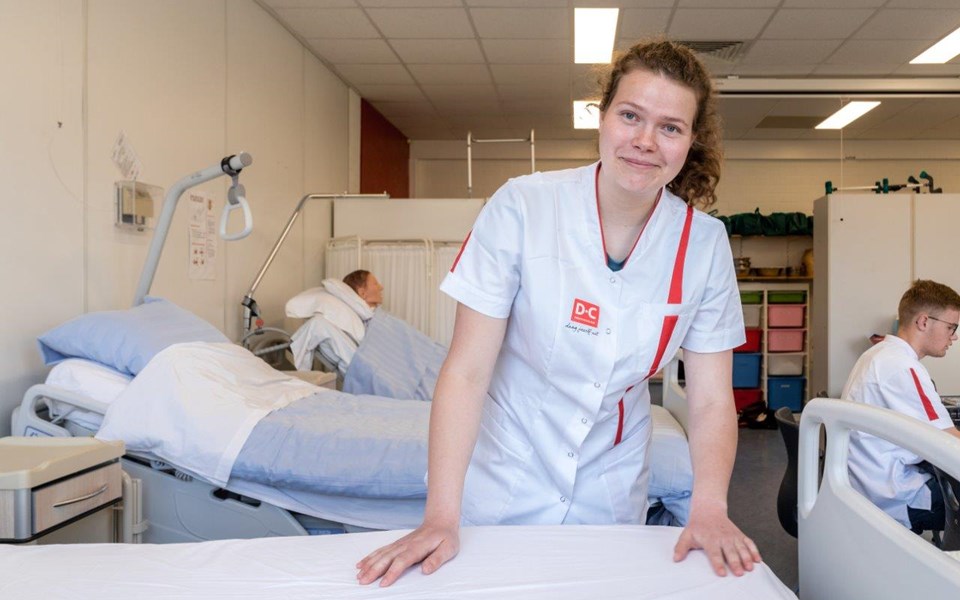 Student opleiding verpleegkunde maakt bed op in zaal. 