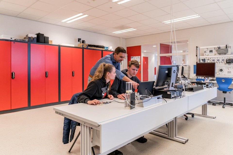 Docent wijst studenten iets aan op laptop
