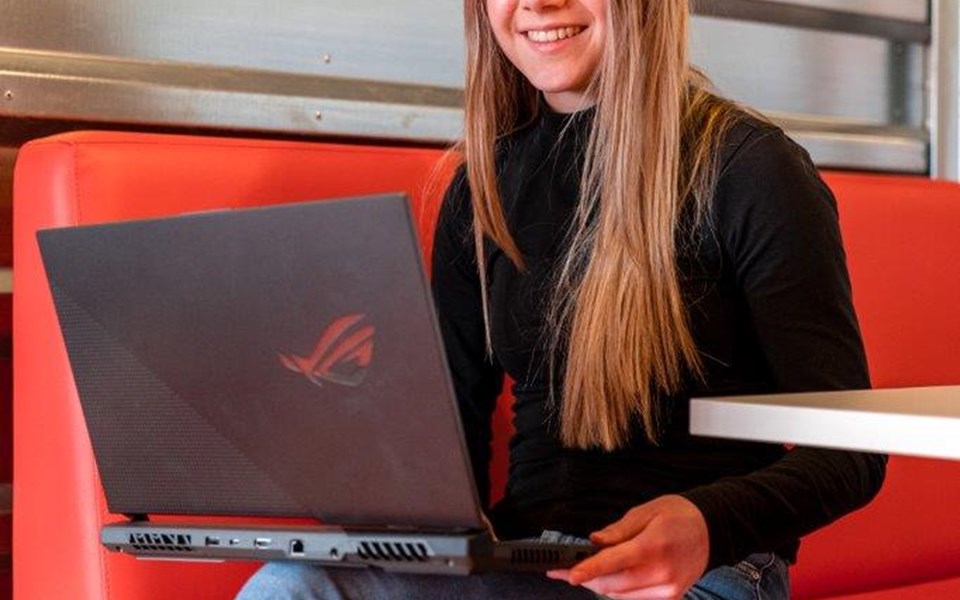 Mediavormgever in opleiding zit met laptop op schoot op rode bank