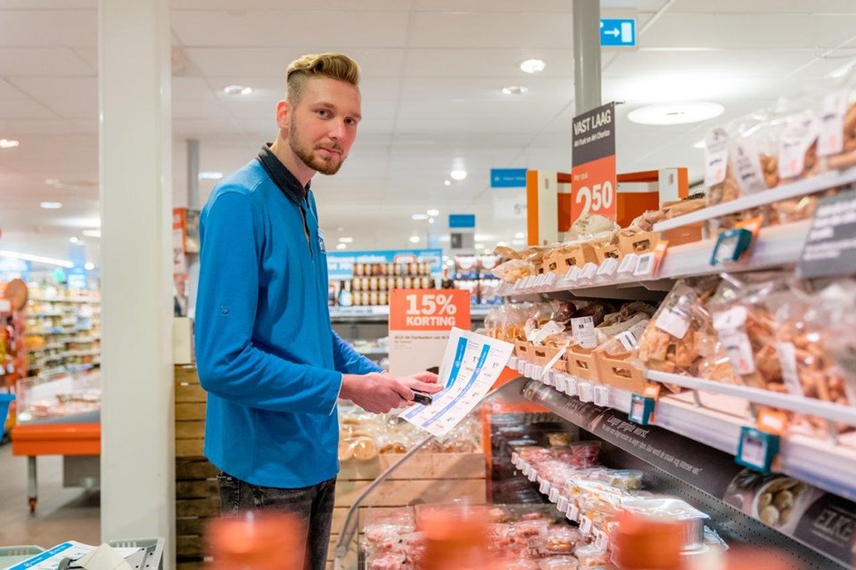 Man staat met lijst bij stelling in supermarkt.