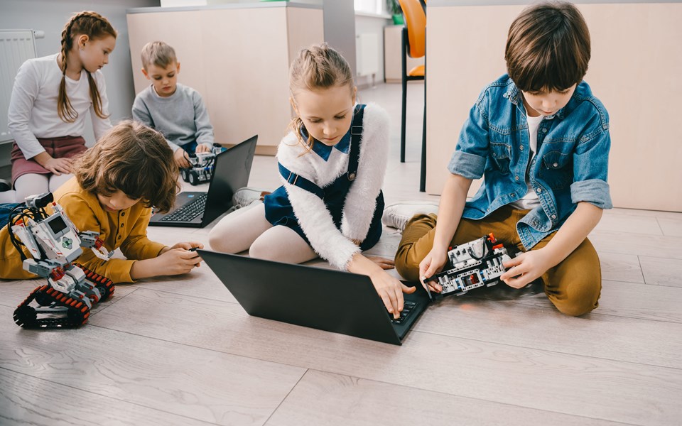 Kinderen op de grond spelend met robots en laptop