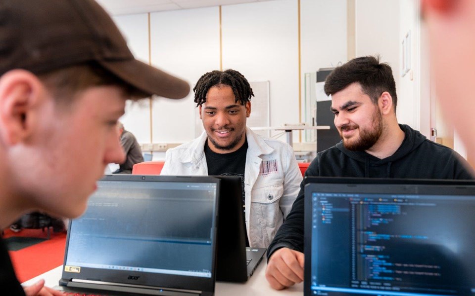 Drie studenten Software Developer zittend lachend te werken achter hun laptop 