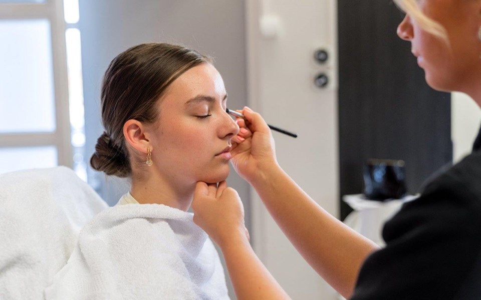 Schoonheidsspecialist in opleiding brengt oog make-up aan met kwast bij klant