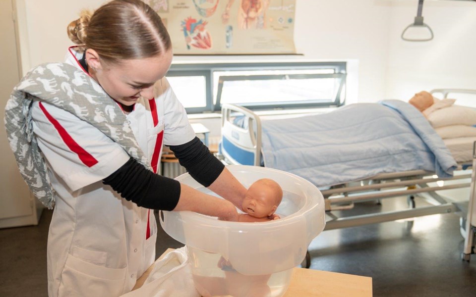Student Helpende doet babypop in tummy tub.