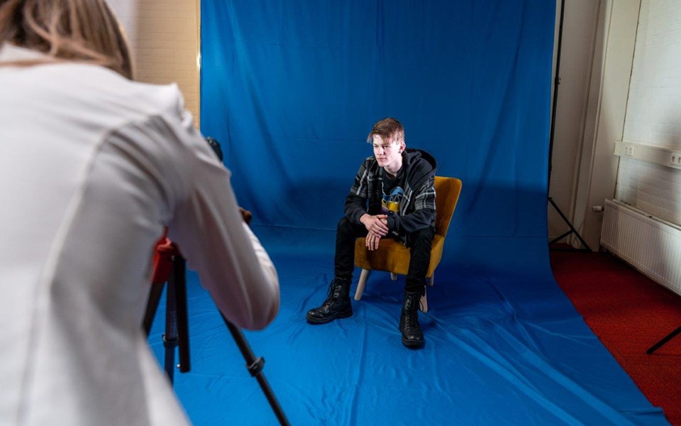 Mediavormgever in opleiding maakt foto's van persoon in stoel op de set