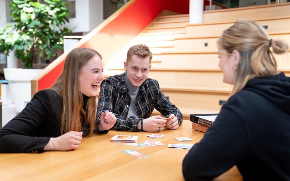 Drie studenten opleiding onderwijsassistent zitten lachend aan tafel tijdens spelen van een spel. 