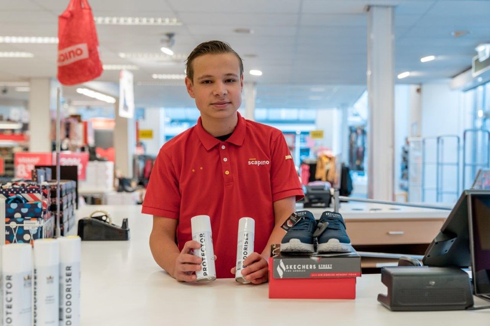 Jongen staat achter de kassen in winkel met schoenen en spray.